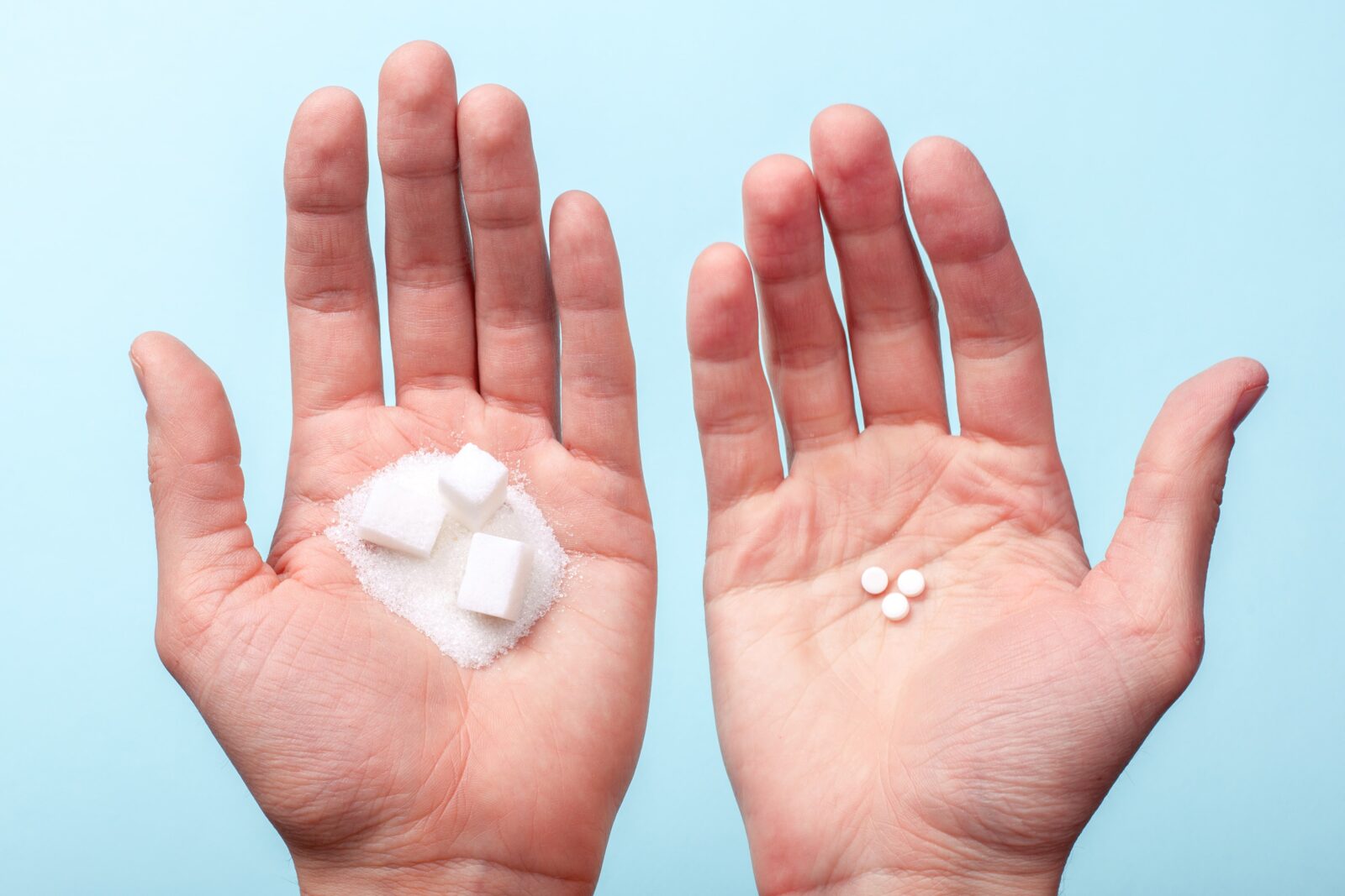 una mano sosteniendo cubos de azúcar y la otra sosteniendo edulcorantes artificiales
